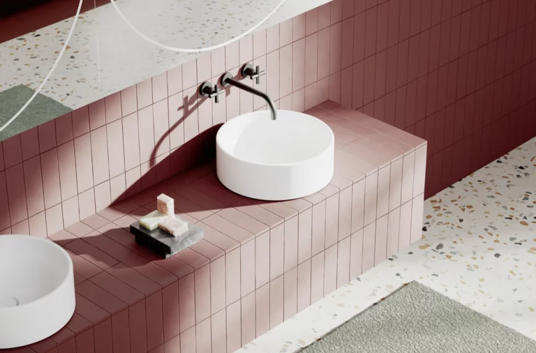 Lavabo moderno sobre encimera roja con grifo mural, espejo y jabonera sobre suelo de terrazo claro.